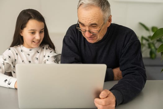 Portrait of senior man and young girl granddaughter using laptop at home