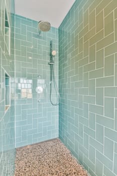 a bathroom with blue and white tiles on the walls, shower head in the corner to the floor is made out of pebbles