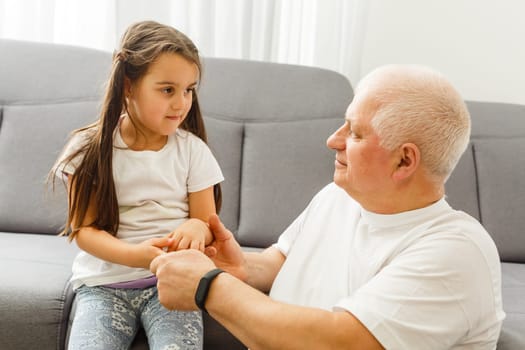 Cute little girl spending time with positive active grandpa in living room.