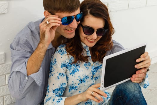 Happy couple pointing finger at digital tablet at home isolated on gray background.