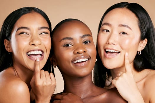 Skincare, beauty and multicultural women smile and point at skin on studio background. Health, wellness and luxury cosmetics, healthy care and happy, beautiful and friendly people with natural makeup.