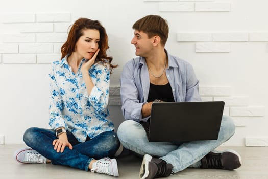 Couple Use Laptop Computer, while Sitting on the Living Floor room of their Apartment. Boyfriend and Girlfriend Talk, Shop on Internet, Choose Product to Order Online, Watch Streaming Service