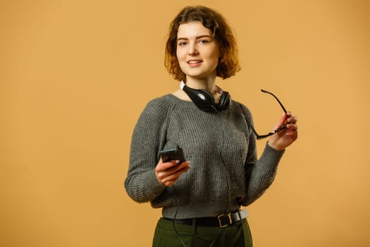 Smiling woman listening music in headphones and using smartphone over yellow background.