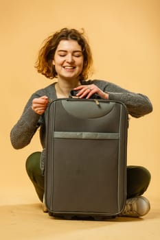 Woman traveler with suitcase on beige background.