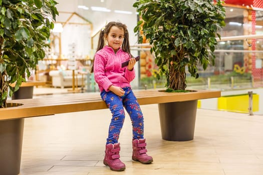 Little child girl playing with smartphone in modern commercial supermarket center
