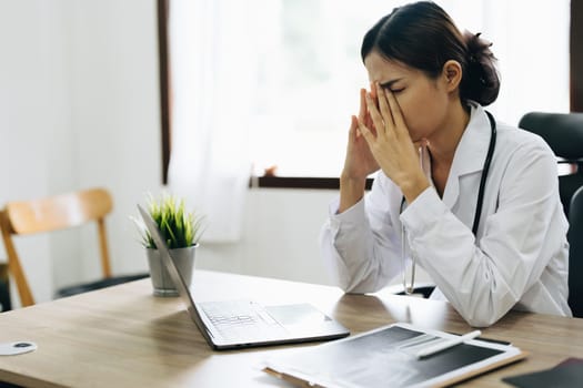 An Asian female doctor uses a computer while showing concern about patient information.