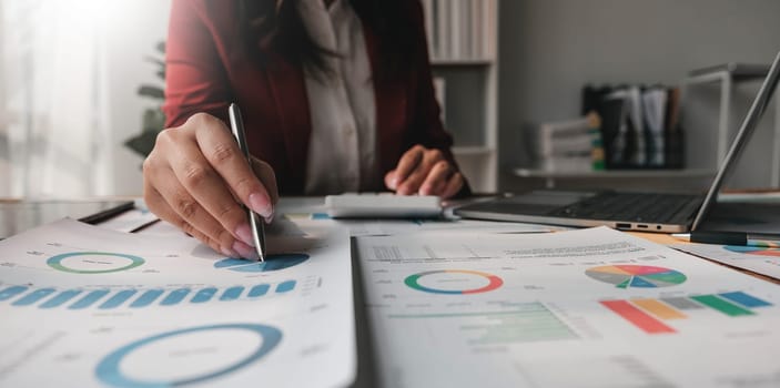 Close up Business woman using calculator and laptop for do math finance on wooden desk in office and business working background, tax, accounting, statistics and analytic research concept