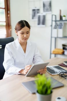 An Asian female doctor is using a tablet computer to analyze patient symptoms before treatment.