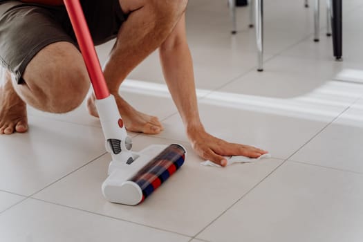 Closeup shot picture white man male sitting and wiping tiled floor with wet wipes holding vacuum cleaner brush head.