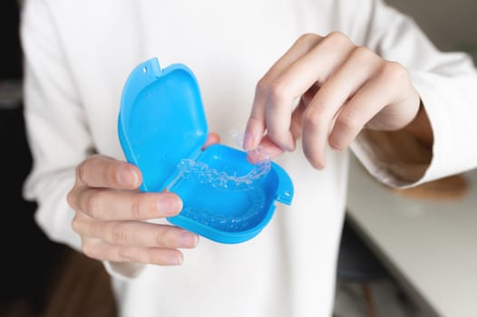 close-up of a young woman, with her hand holding a dental retainer invisible on a cream background of her jacket for the concept of a beautiful teeth treatment course.