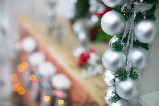 Silver baubles on spruce twigs and decorated fireplace in background.