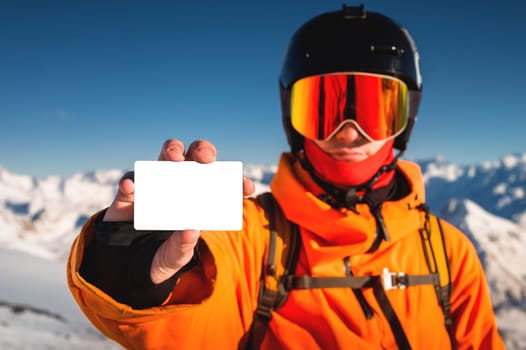 A snowboarder holds an empty lift pass with a mountain in the background. A young man is holding an empty ski pass and looking at the camera. Concept illustrating ski entry fee.
