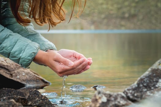 close-up, hands of a girl drinking water from a stream or lake in the mountains. tourist quenches thirst on a hike.
