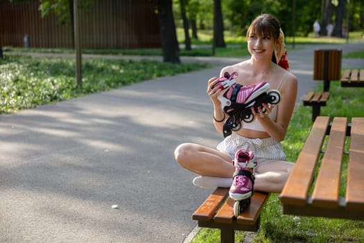 A girl sitting on a bench holds a rollerblade in front of her. A smiling person sits on a park bench with her legs crossed. Spending time outdoors in the park.