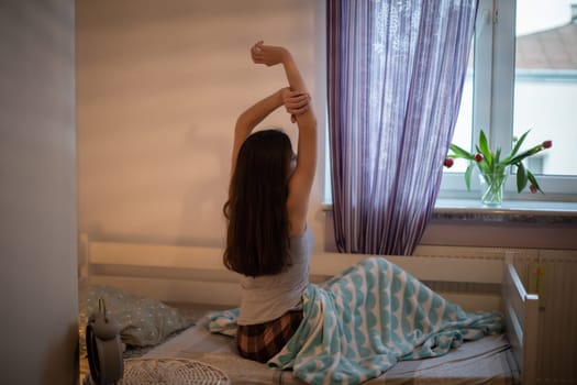 A woman with long hair drags herself and looks out the window. Bright bedroom with decorations.