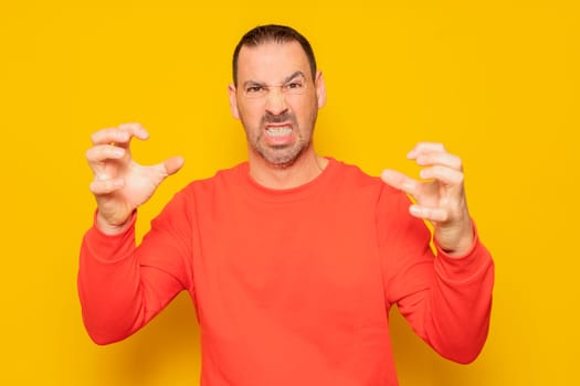 Bearded hispanic man in his 40s wearing a red jumper making claw gesture with an obvious angry, aggressive and thoughtful expression.