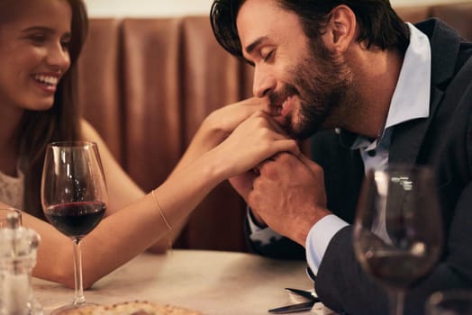 Hand, kiss and date with a couple in a restaurant on a night out together for love, fine dining or luxury. Anniversary, romance and affection with a man kissing his wife while dating in celebration.