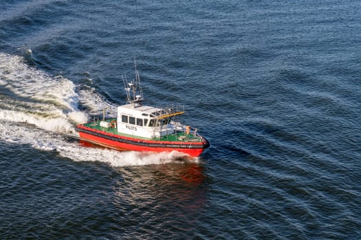 Red pilot boat speeding back to shore after escorting ship from harbor