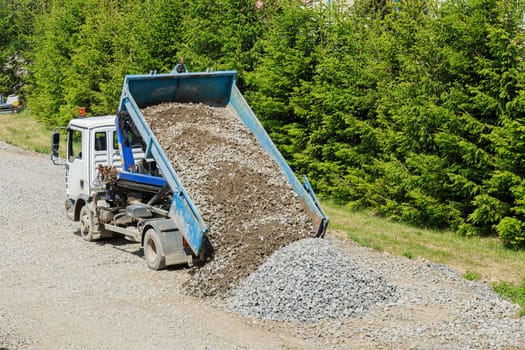 There is a dump truck on a construction site that is dumping gravel on the ground.