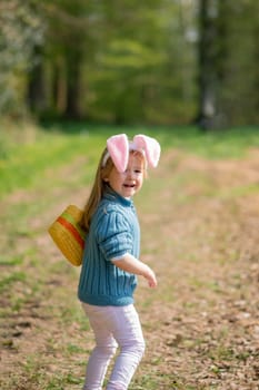 Girl with bunny ears collects chocolate eggs in a basket for Easter