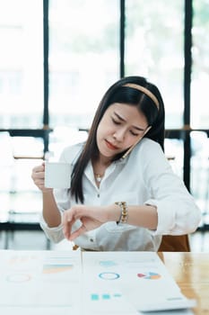 A portrait of a beautiful Asian employee hustle rushing while watch at the clock and talking on the phone.