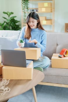 Starting small business entrepreneur of independent Asian woman smiling using computer laptop with cheerful success of online marketing package box items and SME delivery concept.