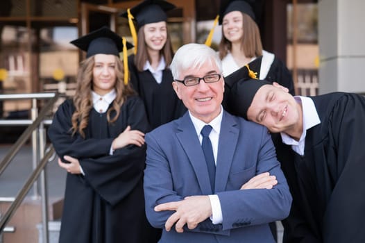 A gray-haired male teacher congratulates students on their graduation from the university