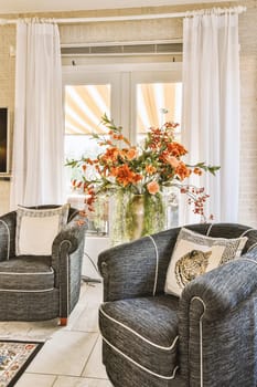 a living room with couches, chairs and flowers in a vase on top of a table next to the window