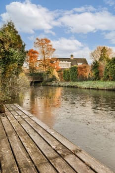 an old wooden bridge over a river in the fall with leaves on the ground and blue sky above, as seen from across the