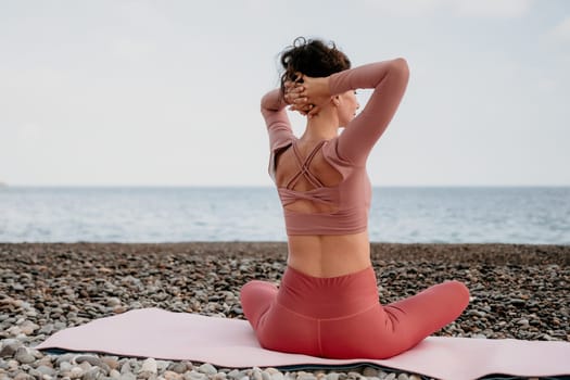 Middle aged well looking woman with black hair doing Pilates with the ring on the yoga mat near the sea on the pebble beach. Female fitness yoga concept. Healthy lifestyle, harmony and meditation.