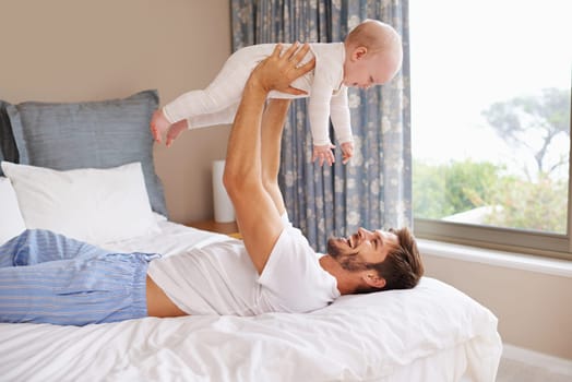 Its important for a father and son to bond. a father lying on a bed holding his baby girl up in the air