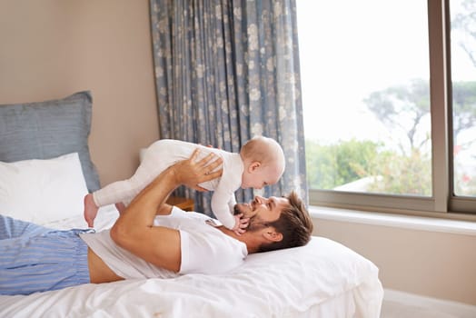 Face to face with daddy. a father lying on a bed holding his baby girl up in the air