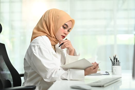 Focused muslim woman manager wearing a hijab checking his working schedule plan at her working desk.