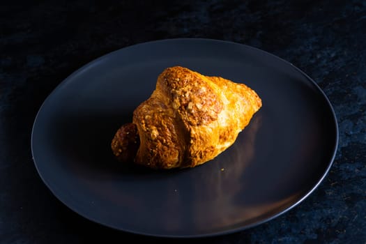 Freshly backed french croissant shiny in the rays of morning sun, dark background, kitchen