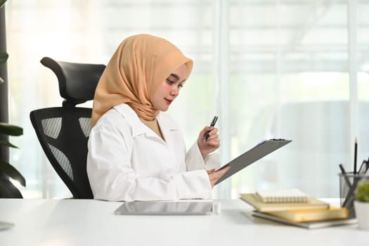 Portrait of muslim businesswoman sitting in her office and reading information on document.