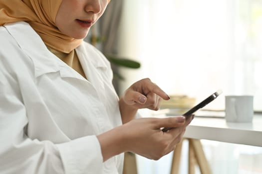 Young modern muslim woman in hijab typing messages or surfing internet on smart phone.