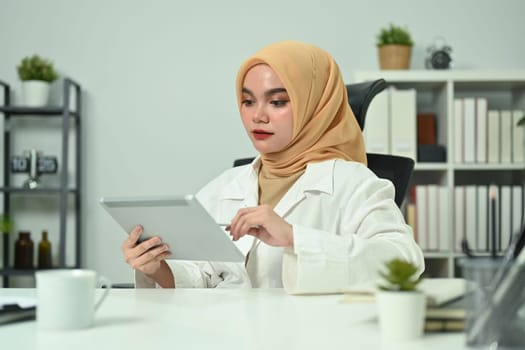 Beautiful Asian muslim businesswoman checking email on digital tablet, working at her workstation.