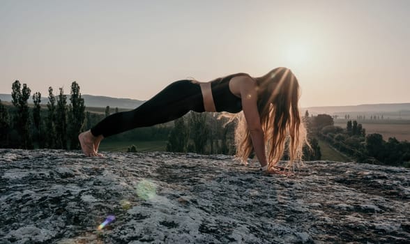 Well looking middle aged woman with long hair, fitness instructor in leggings and tops doing stretching and pilates on the rock near forest. Female fitness yoga routine concept. Healthy lifestyle.