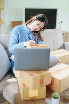 Starting small business entrepreneur of independent Asian woman smiling using computer laptop with cheerful success of online marketing package box items and SME delivery concept.