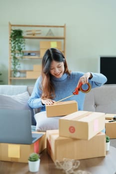 Starting small business entrepreneur of independent Asian woman smiling using computer laptop with cheerful success of online marketing package box items and SME delivery concept.