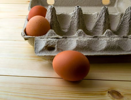 Three eggs in a carton. Three eggs in a cardboard box on a wooden table.