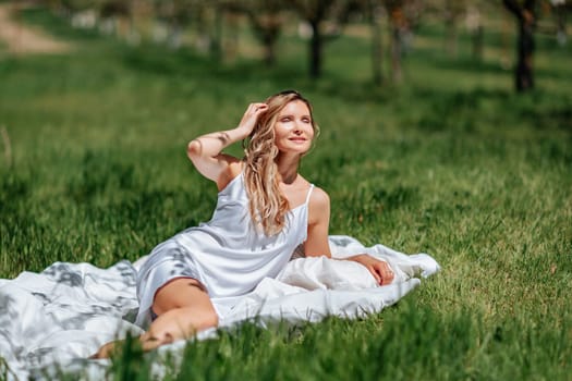 woman sleeps on a white bed in the fresh spring grass in the garden. Dressed in a blue nightgown