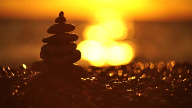 Balanced rock pyramid on pebbles beach. Golden sea bokeh on background. Selective focus, zen stones on sea beach, meditation, spa, harmony, calm, balance concept