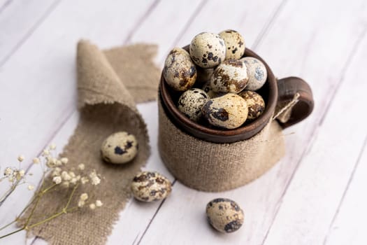 Fresh quail eggs in a clay mug on the table. Bright spring festive background and a branch of gypsophila. Close-up. Healthy eating. Easter. side view from the top