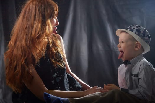 Woman with boy in hat. Mom with son on a dark background. Family portrait with mother with red hair and boy having fun together