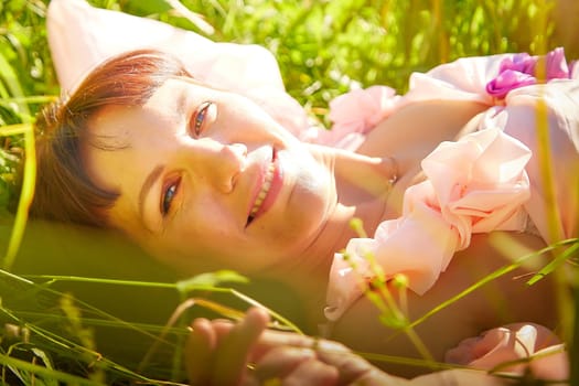 Beautiful girl in lush pink ball gown in green field during blooming of flowers and blue sky on background. Model posing on nature landscape as princess from fary tale