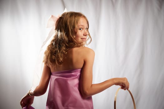 Portrait of cute kid girl posing in pink beautiful dress on white background. Model in studio looking as gentle magic princess from fairy taly having photo shoot on white background