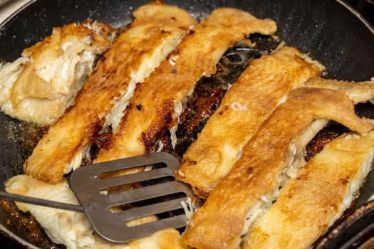 the cook checks the readiness of the fish with a fork. delicious pieces of fried flounder in a frying pan. Cooking fish. Supper. Healthy eating. Seafood