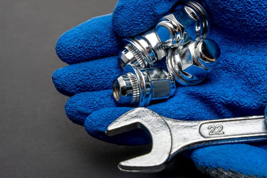 Shiny new wheel nuts and a wrench in the hand of a car mechanic in a blue protective glove . Auto parts and auto repair. Car maintenance. copy space