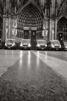 Grayscale shot of row of Mercedes-Benz Sprinter police cars in front of Cologne Cathedral in Germany